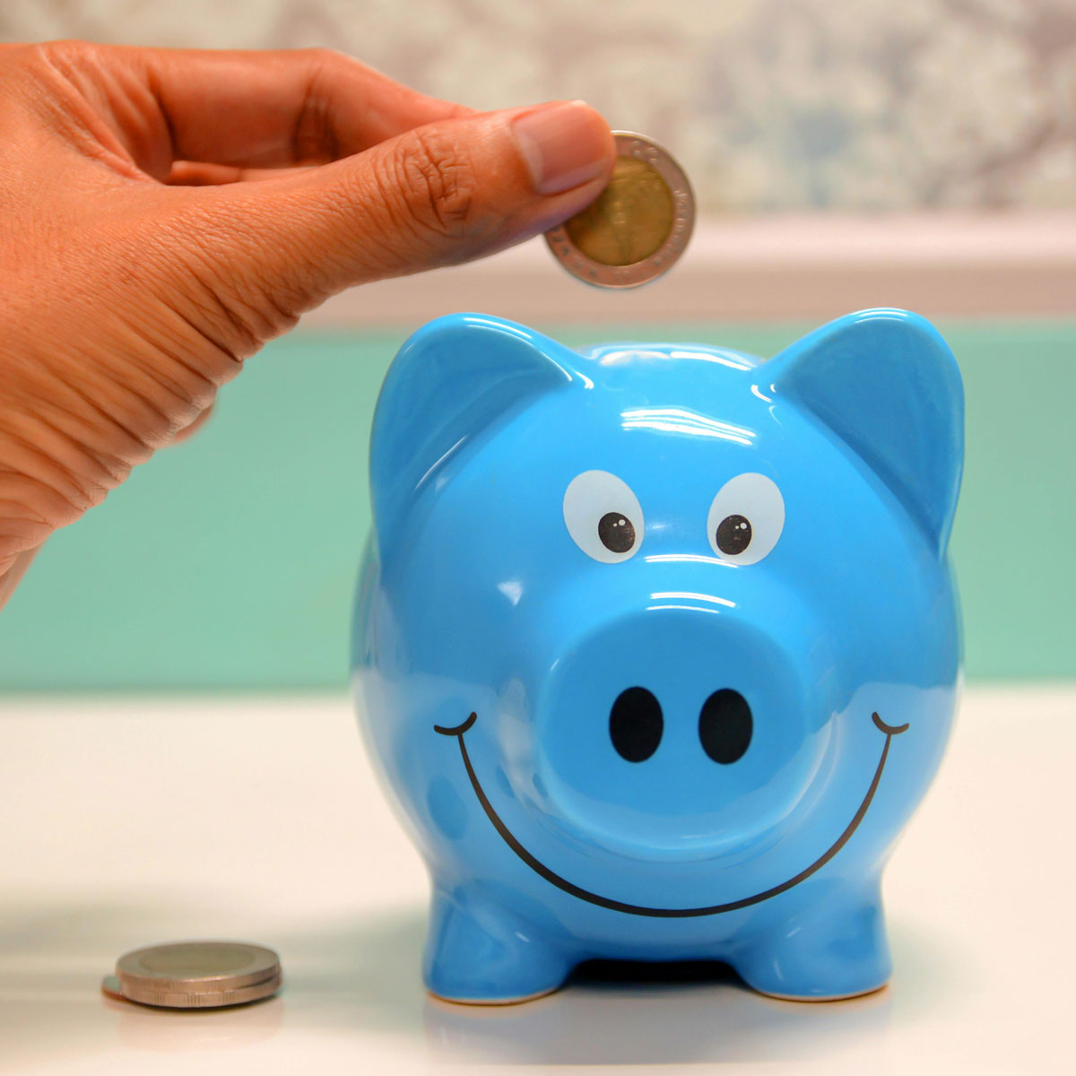 מחשב נייד זול - תמונה של יד משלשלת מטבע לקופת חיסכון כחולה בצורת חזיר